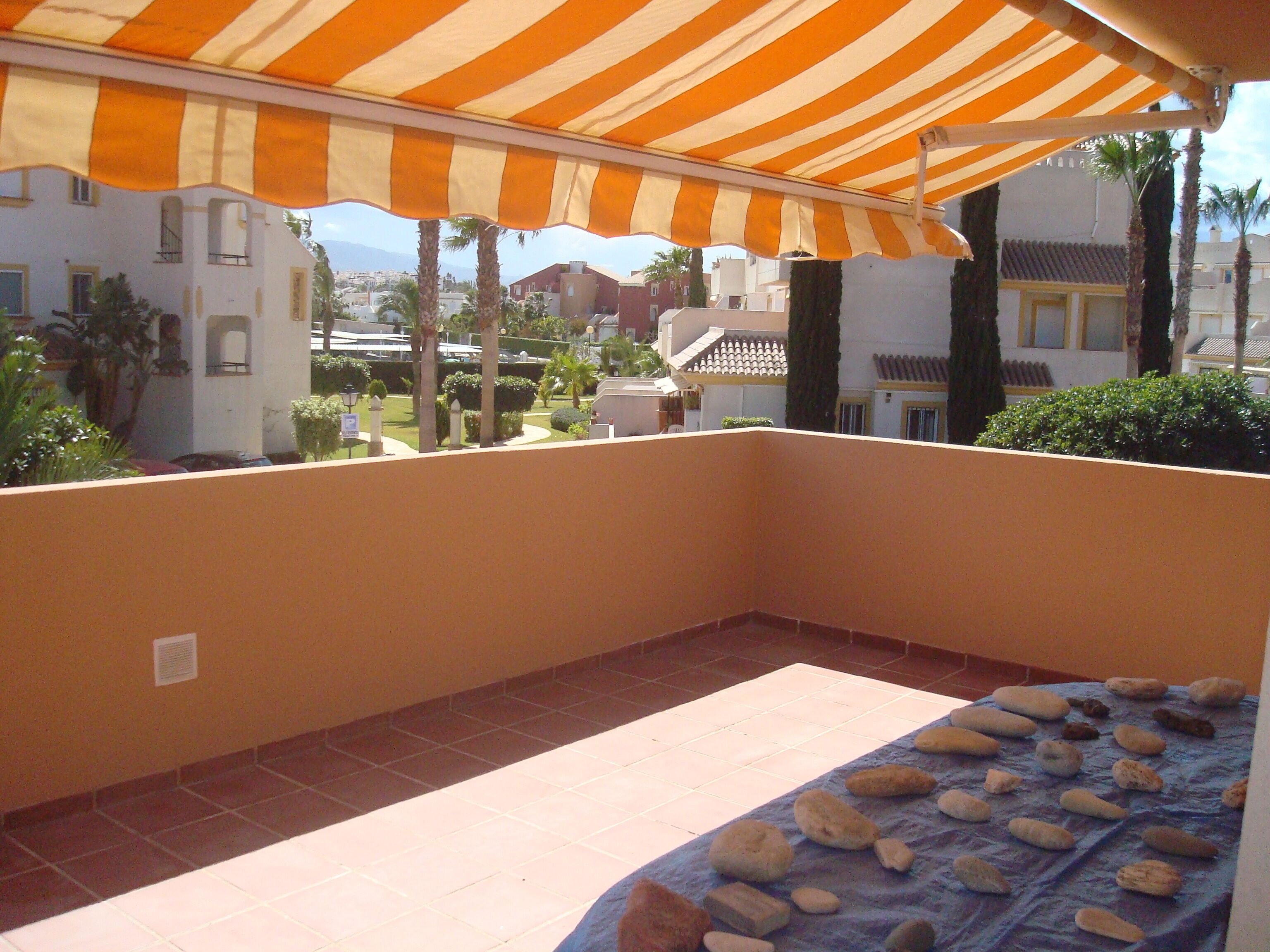 A balcony with a striped awning, tiled floor, and a bed with a blue cover.