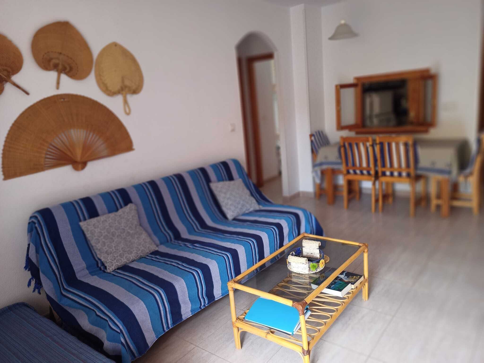 A living room with a striped sofa, a glass coffee table, and a dining area with chairs and a table.