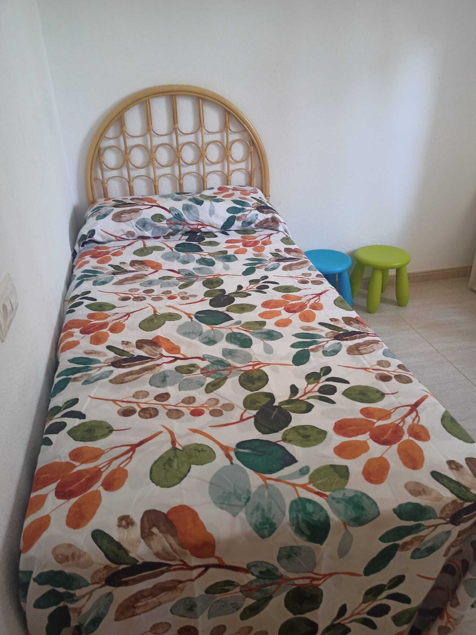 A single bed with a wooden headboard, a colorful floral bedspread, and two small stools.