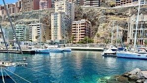 Ένα λιμάνι με αγκυροβολημένα σκάφη, καθαρά νερά και κτίρια στο βάθος.