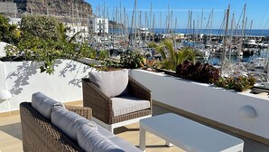A terrace with wicker furniture, a white table, and a view of a marina with boats. - Frontline Marina Apartment With Private Roofterrace and Seaview by El Sirocco (Mogan)