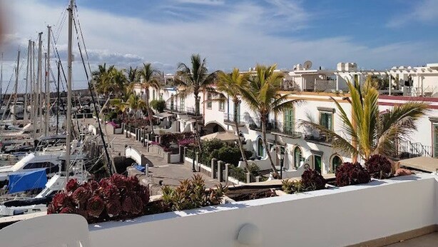 A marina with boats, palm trees, and white buildings with balconies. - Frontline Marina Apartment With Private Roofterrace and Seaview by El Sirocco (Mogan)