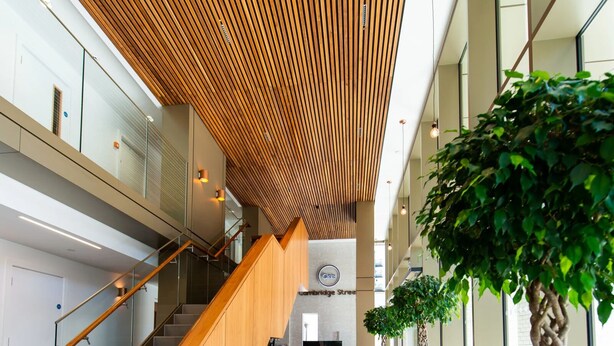A spacious lobby with a wooden staircase, large potted plants, and a reception desk. - The Assembly (Manchester)