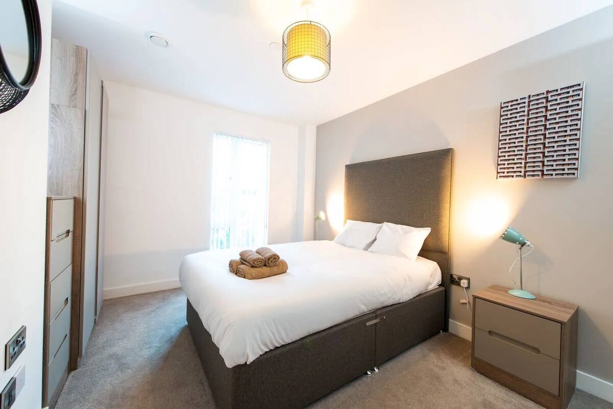 A modern bedroom with a large bed, bedside tables, a wall-mounted light, and a window.