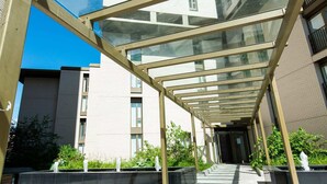 A covered walkway with glass panels and a tiled floor leading to a building entrance. - The Assembly (Manchester)