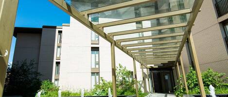 A covered walkway with glass panels and a tiled floor leading to a building entrance.