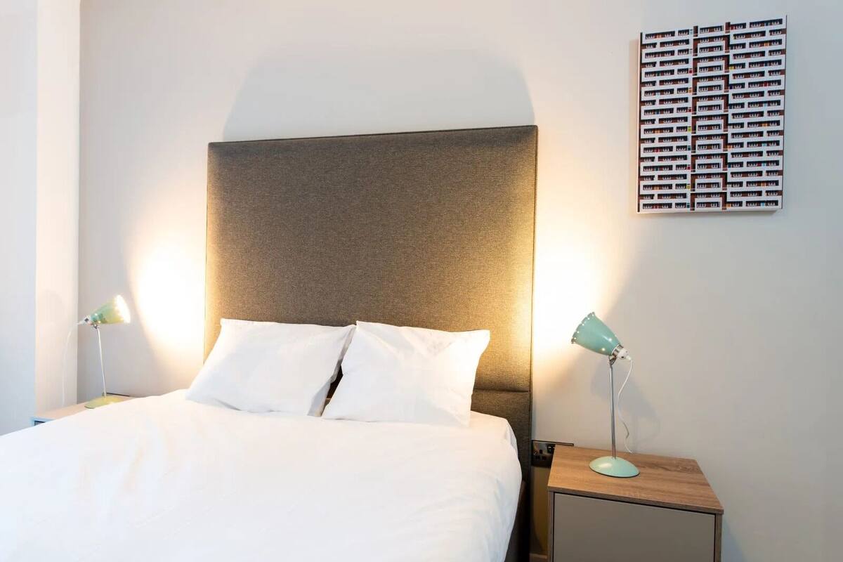 A neatly made bed with white linens, a headboard, and two bedside tables with lamps.