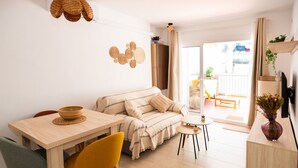 A modern living space with a sofa, dining table, chairs, a small side table, a television, and a balcony with plants. - Terrace Retreat -stay in the Heart of Sitges (Sitges)