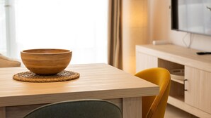 A wooden table with a bowl on a woven placemat, a yellow chair, and a television on a wooden cabinet. - Terrace Retreat -stay in the Heart of Sitges (Sitges)