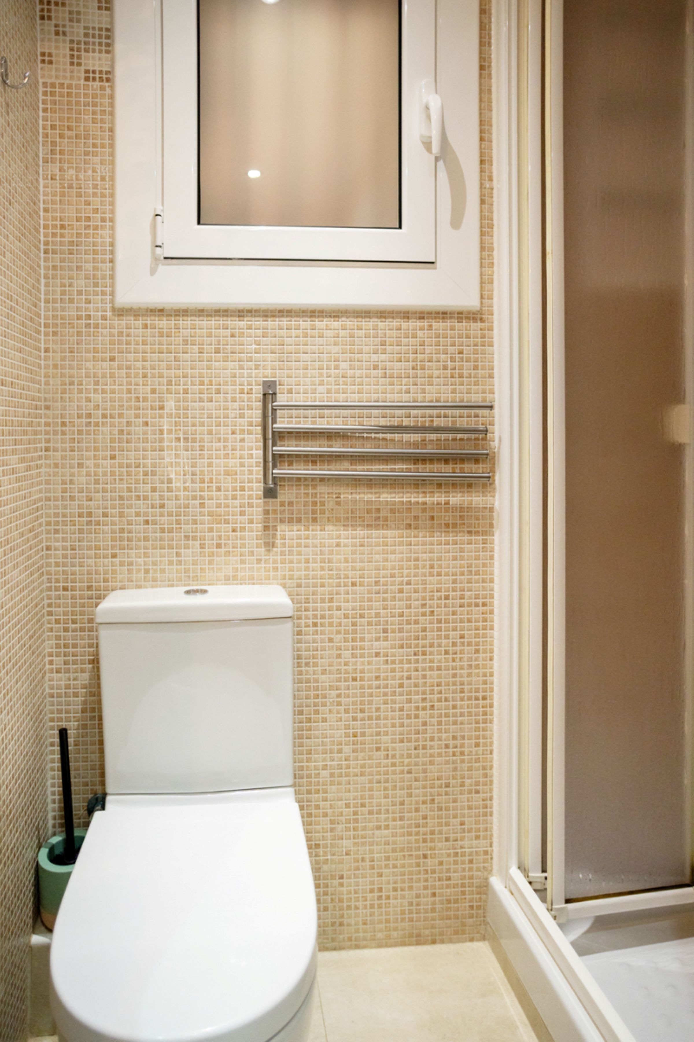 Un baño con inodoro, ducha y ventana sobre el inodoro.