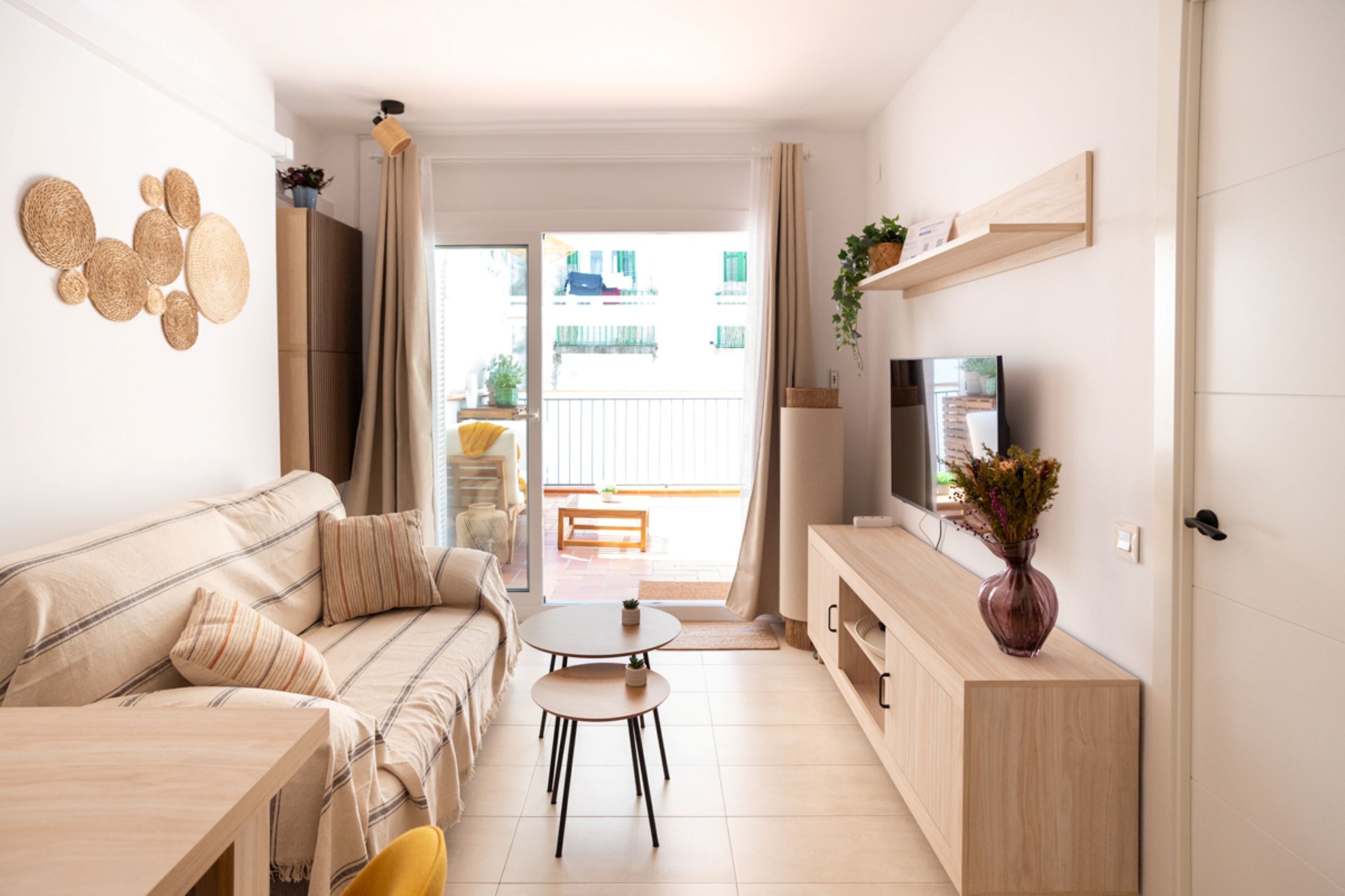 A modern apartment with a sofa, a small dining table, a TV, and a balcony with a view.