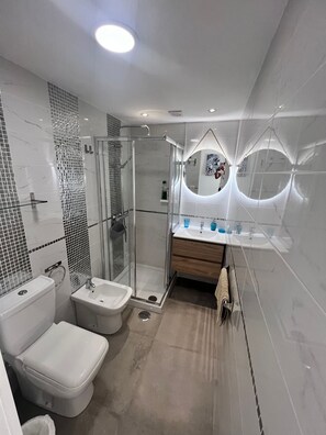 A modern bathroom with a glass-enclosed shower, a white toilet, a sink, and a vanity with a mirror. - Oceanfront Condo in Playa las Americas With Sea Views (Arona)