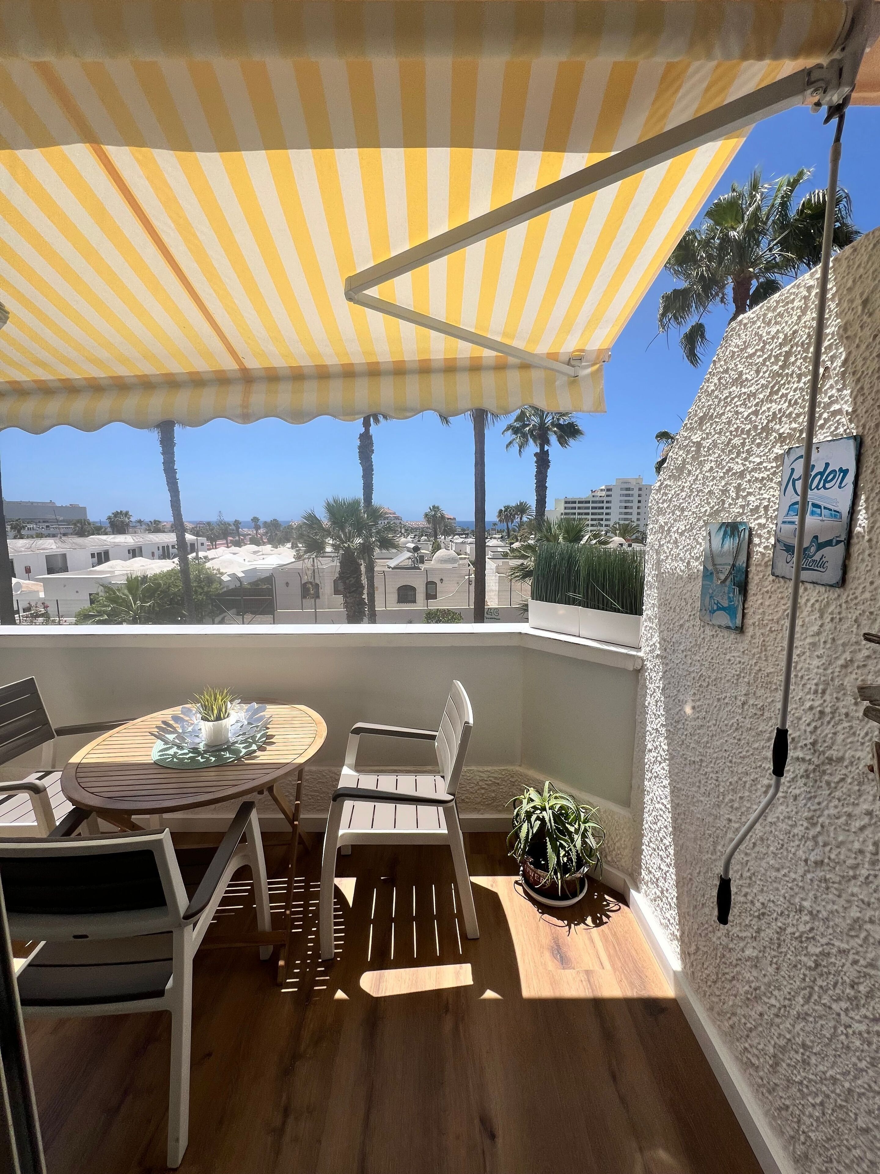 A balcony with a striped awning, wooden furniture, a potted plant, and a view of the cityscape.