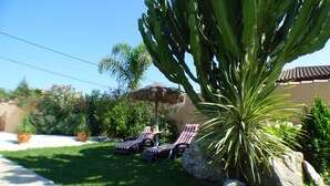 A garden with a large cactus, two lounge chairs, and a thatched umbrella. - Rural House With Private Pool, new and Beautiful Garden (Conil de la Frontera)