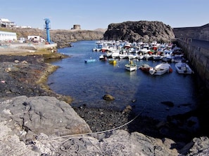A rocky harbor with numerous boats docked, a lighthouse, and a large rock formation in the background.