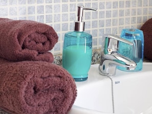 A bathroom with a white sink, a chrome faucet, a blue soap dispenser, and rolled towels.