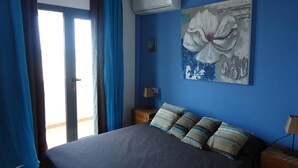 A bedroom with a bed, blue curtains, an air conditioning unit, and a painting of a flower on the wall. - Bravo´s Aparment Cotillo 1 (La Oliva)