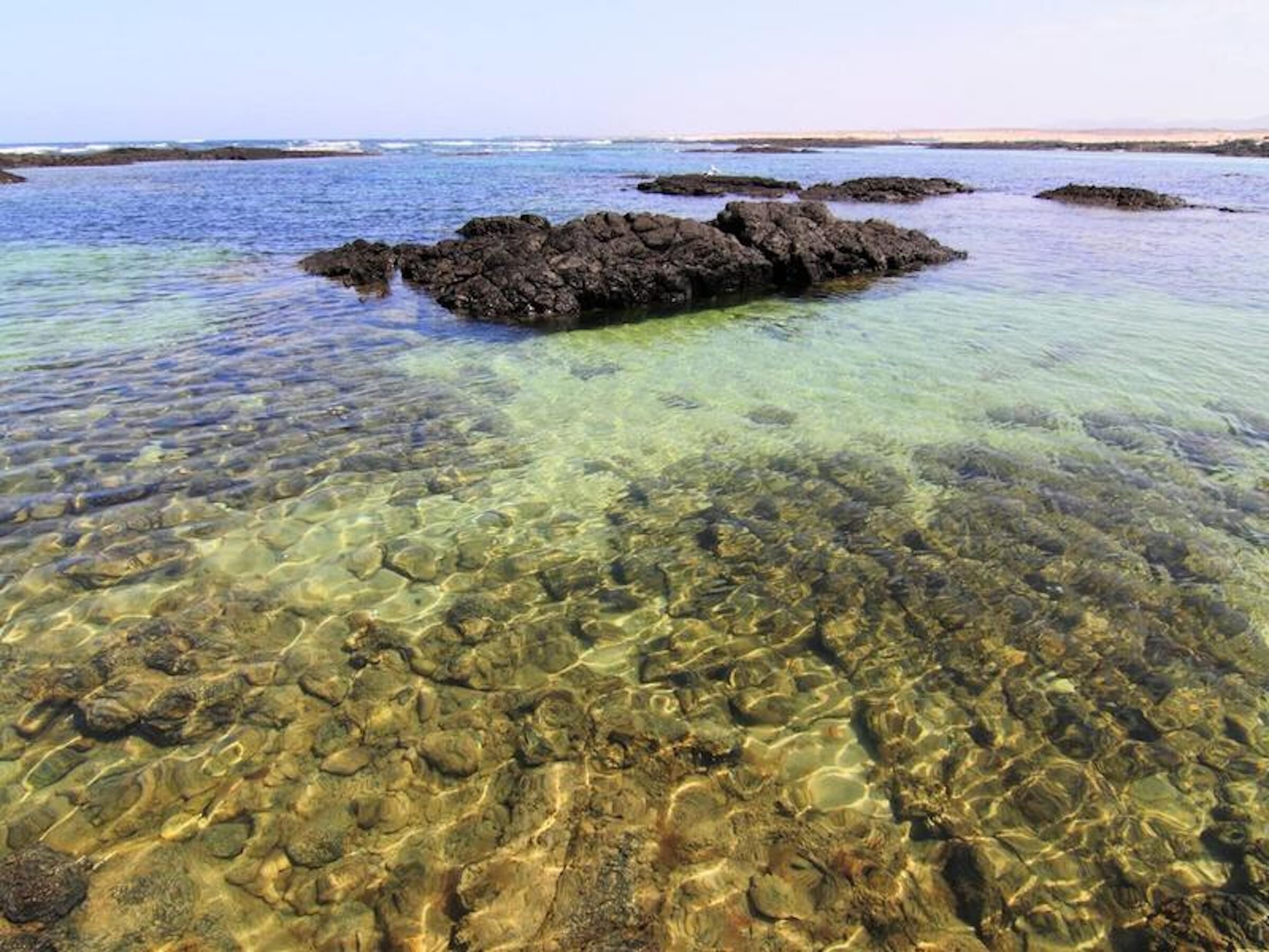 A clear coastal area with rocky formations and shallow water.