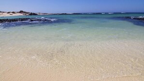 Una playa con aguas poco profundas y cristalinas y una orilla arenosa.