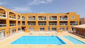 A hotel with a large outdoor swimming pool, multiple balconies, and sun loungers.