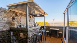 A stone bar with a view of the water, outdoor seating, and a glass-enclosed balcony. - Oceanum Visum Spa Deluxe (Puerto Real)