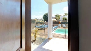 En vy från ett rum ut mot ett utomhusområde med en pool, solstolar och en pool.