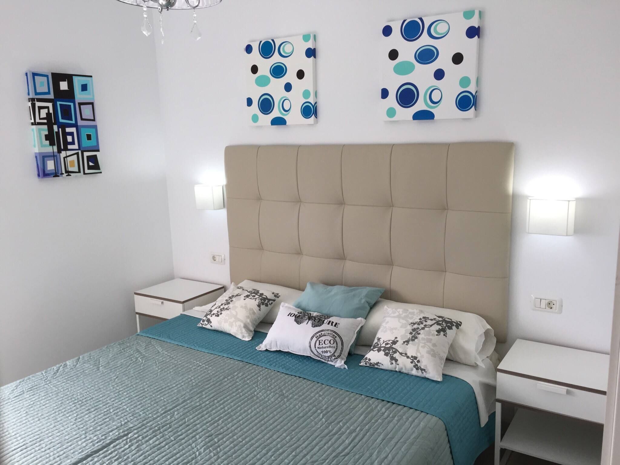 Ein Schlafzimmer mit einem Bett, zwei Nachttischen, einer Chandelierleuchtre und Wandbildern.
