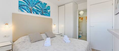 A hotel room with a bed, a ceiling fan, a painting, and a bathroom door.