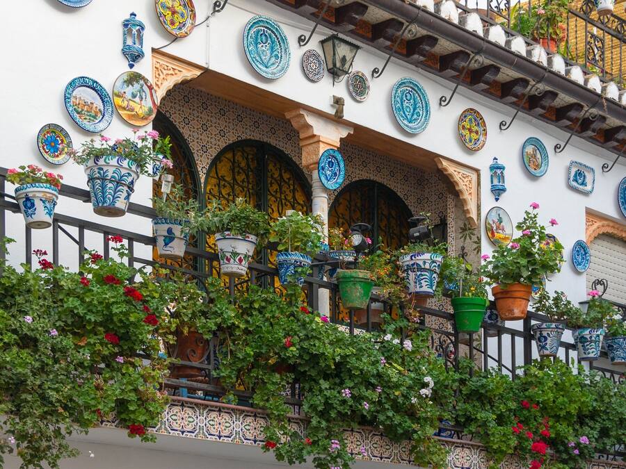 Fachada de edificio con intrincados trabajos en azulejos, varias plantas en macetas y barandilla de balcón.