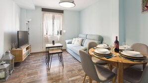 A dining area with a wooden table set for four, a sofa, and a television on a stand. - Sky is Blue in Granada (Granada)