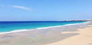 A wide beach with clear blue water and a distant shoreline.