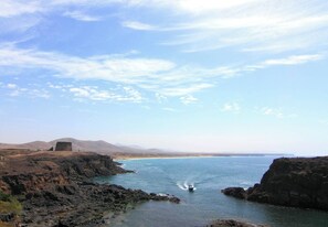 A coastal landscape with rocky terrain, a body of water, and distant mountains.