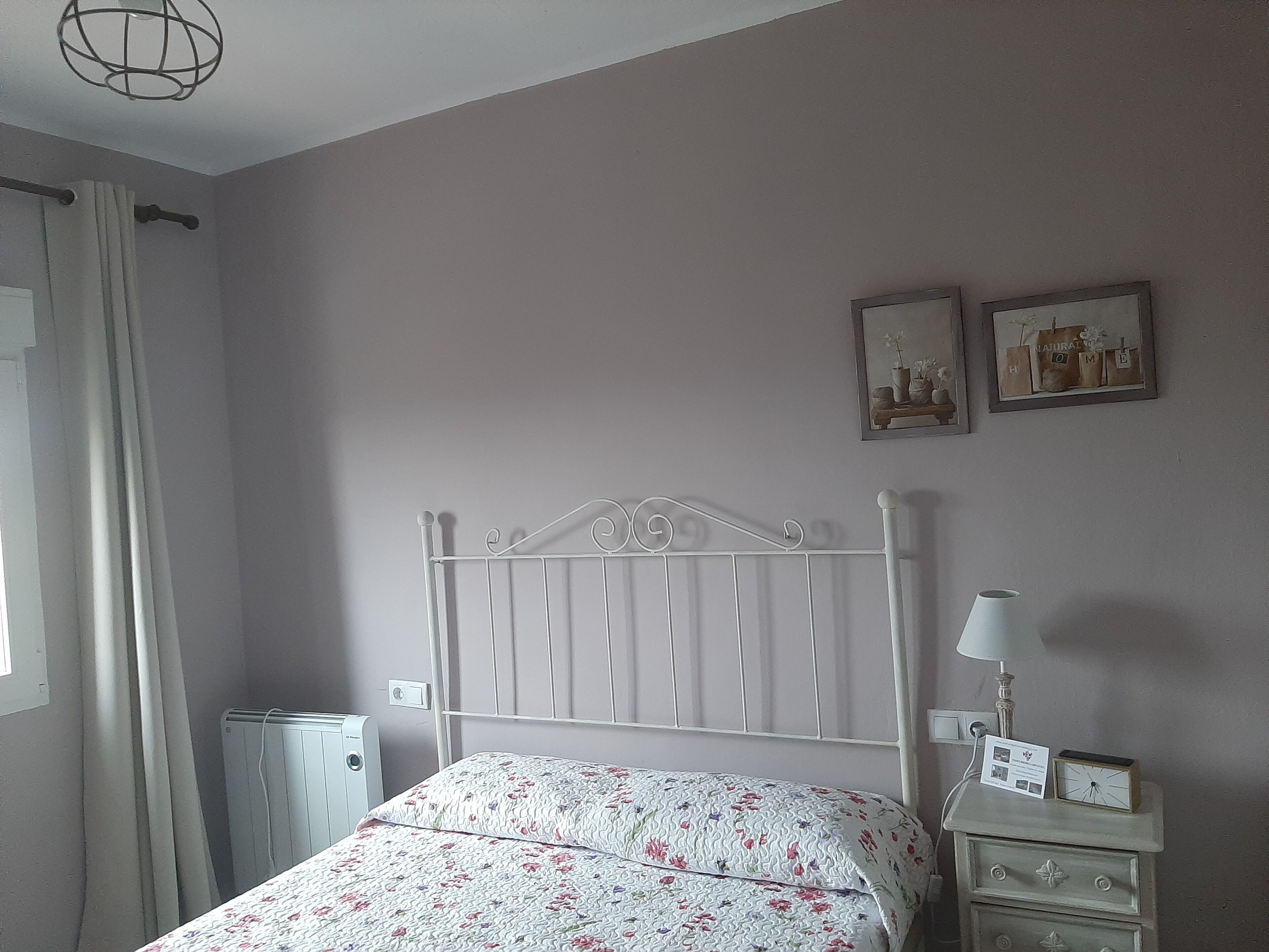 Una camera da letto con un letto, un comodino, una lampada e due quadri appesi al muro.