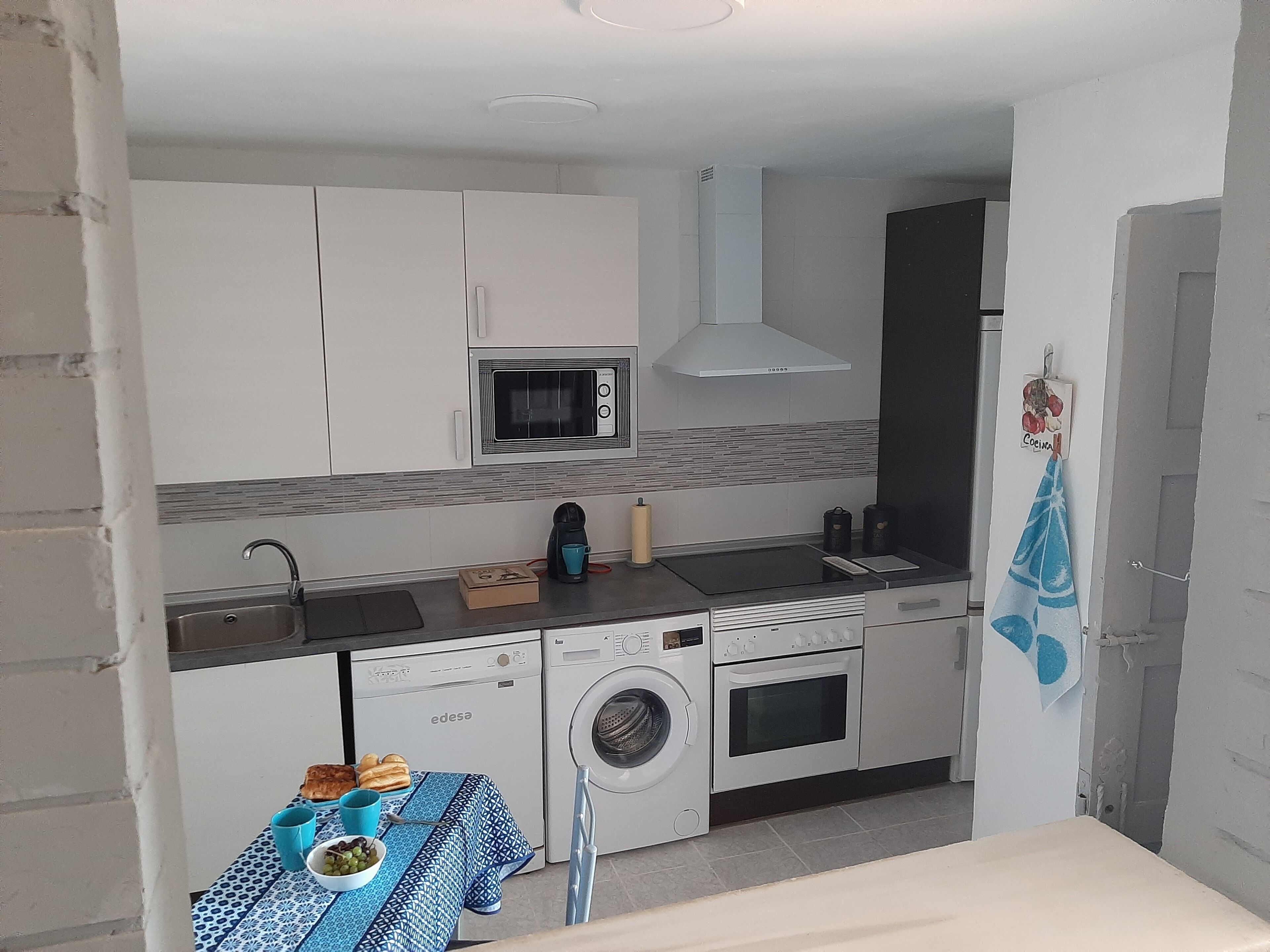 Una cocina compacta equipada con microondas, horno, lavadora y una pequeña mesa con alimentos.