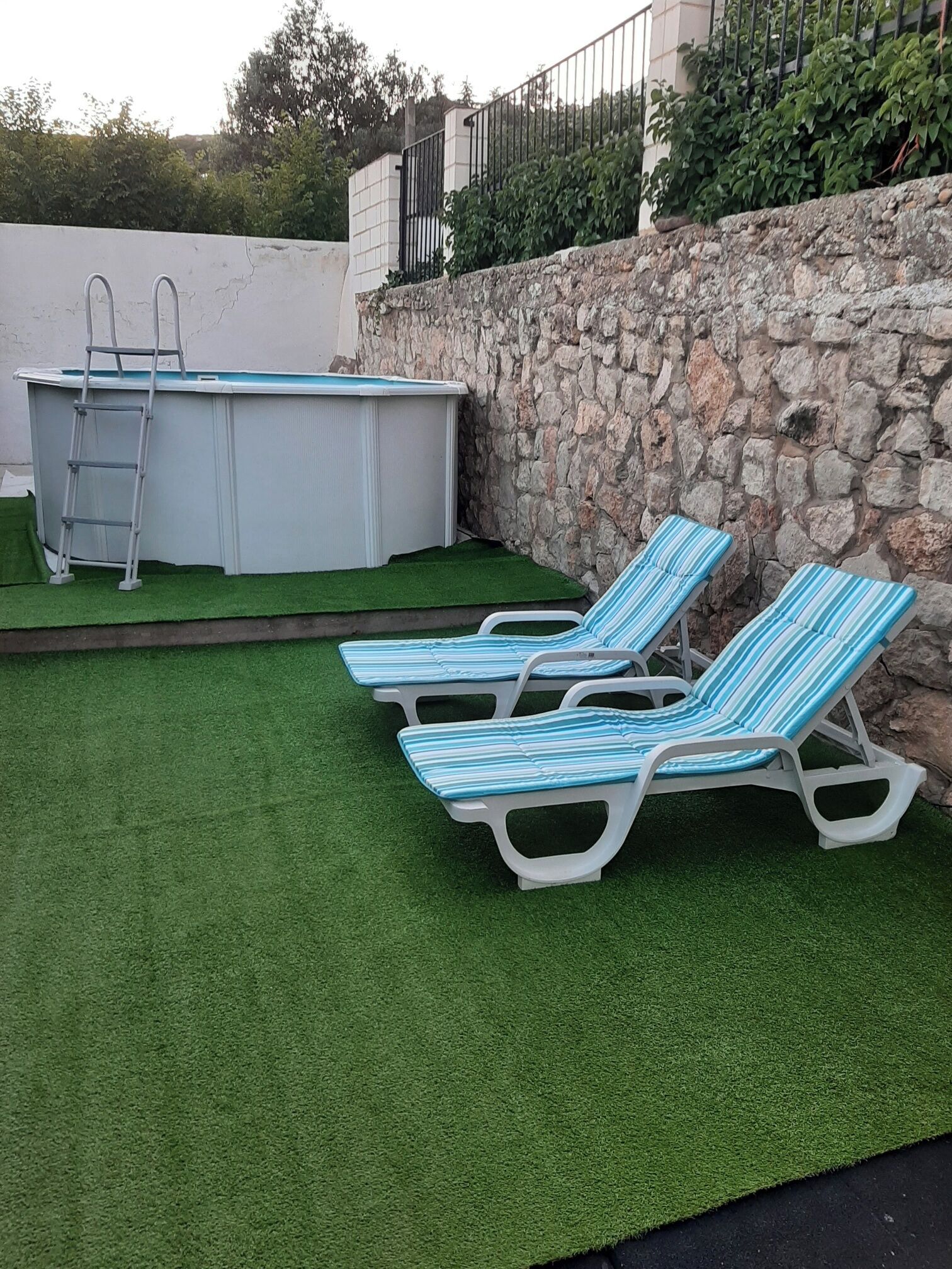 Ein Garten mit Kunstgrasanlage, einem Swimmingpool und zwei Liegestühlen.