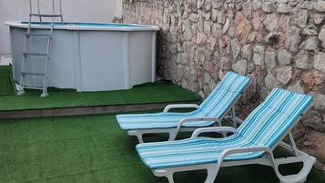 Ein Garten mit Kunstgrasanlage, einem Swimmingpool und zwei Liegestühlen.
