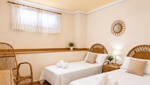 A hotel room with two beds, a wicker chair, a bedside table with a lamp, and a window with curtains. - Beachfront Home La Mata (Torrevieja)