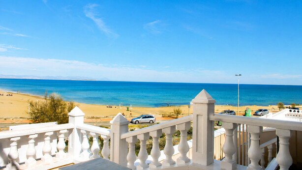 A balcony with a view of the beach, cars parked on the street, and a clear blue sky. - Beachfront Home La Mata (Torrevieja)