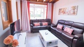 Un salón con un sofá de cuero marrón, una mesa de centro blanca y un televisor sobre un mueble.