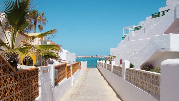 Un paseo marítimo con edificios blancos, palmeras y vista al mar.