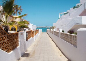 Um passeio marítimo com edifícios brancos, palmeiras e vista para o mar.