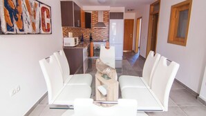 Una cocina moderna con microondas, estufa y refrigerador. Hay un comedor con mesa de vidrio y sillas blancas.
