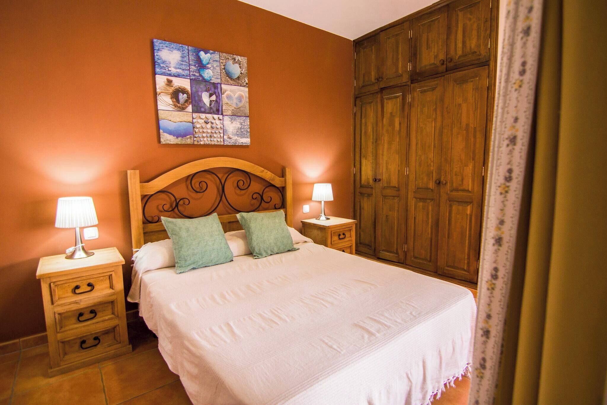 Een slaapkamer met een groot bed, twee nachtkastjes met lampen, een houten garderobe en een kunstwerk aan de muur.