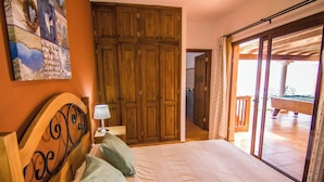 Un dormitorio con cama, un armario de madera, un cuadro en la pared y un balcón con piscina.