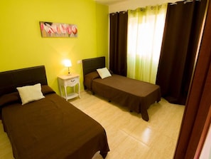 A room with two single beds, a nightstand with a lamp, a painting on the wall, and curtains on the window. - Villa In Corralejo,fuerteventura (La Oliva)
