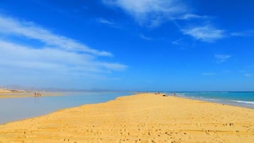 A wide sandy beach with clear blue water and a few people in the distance.