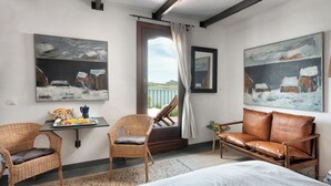 A room with a bed, two wicker chairs, a leather sofa, a small table with breakfast items, and two paintings. - 1st Floor Apartment In Old Lakeside Andalusian Farmhouse (Antequera)