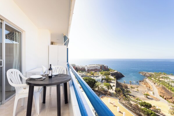 A balcony with a table and chairs, overlooking a coastal view with buildings and the sea. - Playa Paraiso - Exceptional Ocean-sunset View - Pool-wifi-smart TV (Adeje)