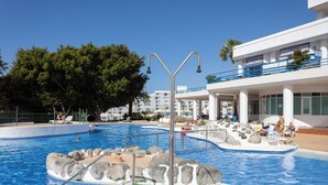 A swimming pool with a rock feature, lounge chairs, and a building with balconies. - Playa Paraiso - Exceptional Ocean-sunset View - Pool-wifi-smart TV (Adeje)