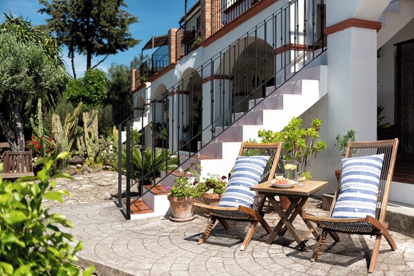 Un patio amueblado con mobiliario exterior, plantas en macetas y una escalera que lleva a un nivel superior.